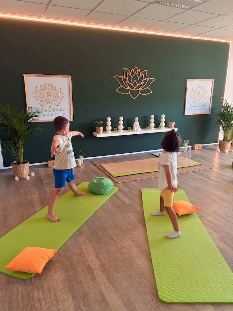 Zwei Kinder stehen barfuß auf grünen Yogamatten im Kursraum der Lebensleicht Akademie